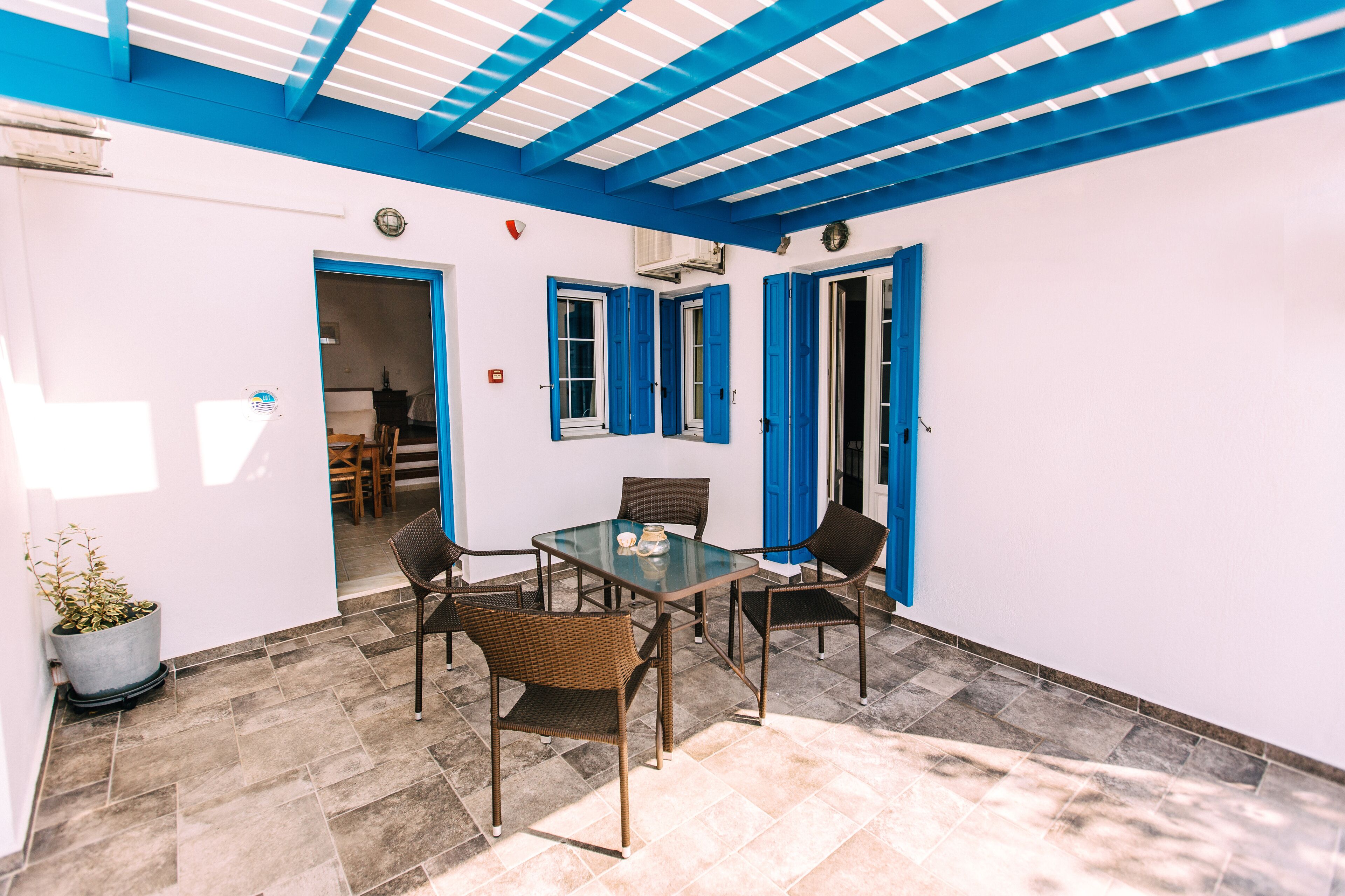 A patio area with a glass table and wicker chairs, a potted plant, and a blue ceiling.