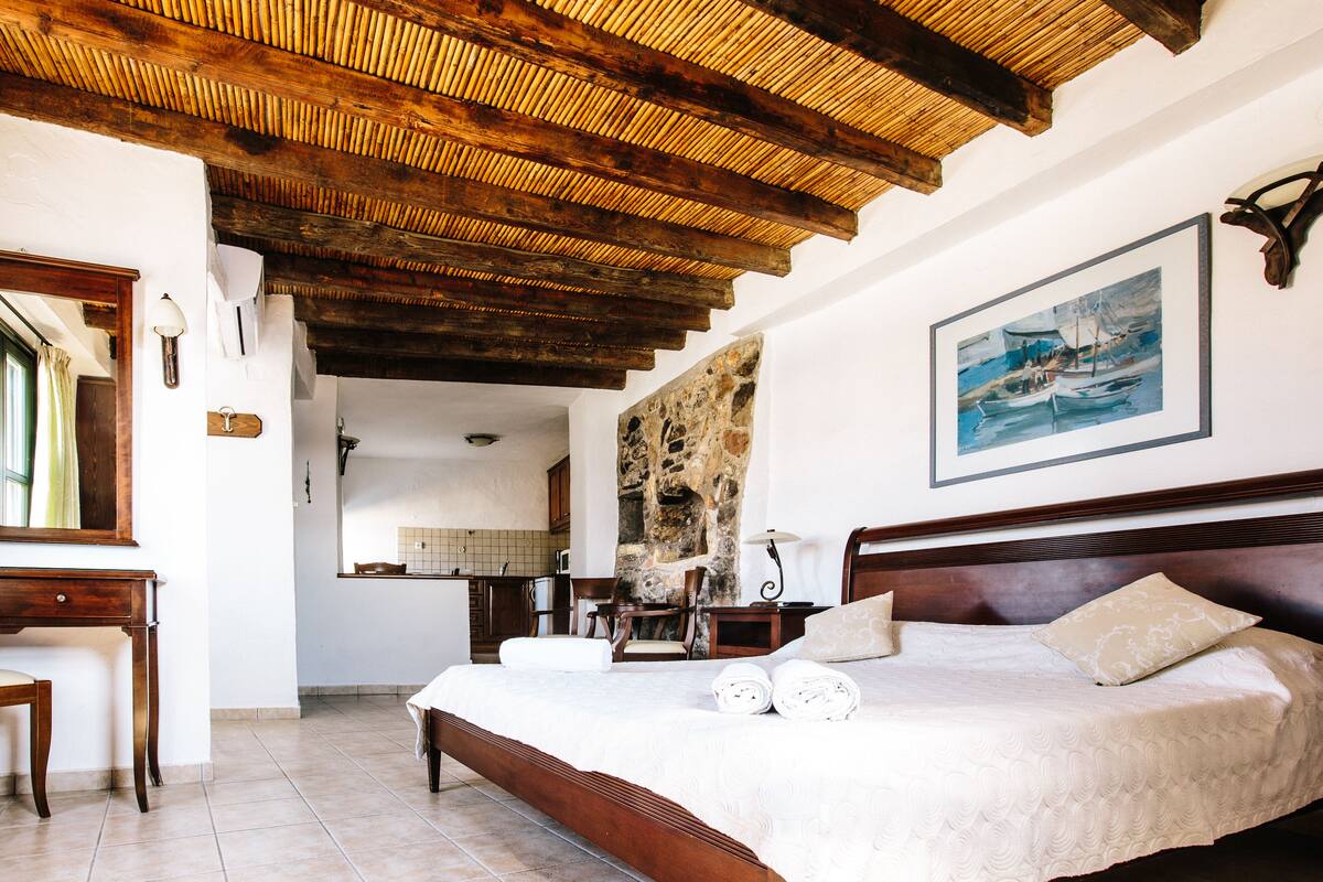 A bedroom with a wooden ceiling, a bed with white linens, and a painting on the wall.