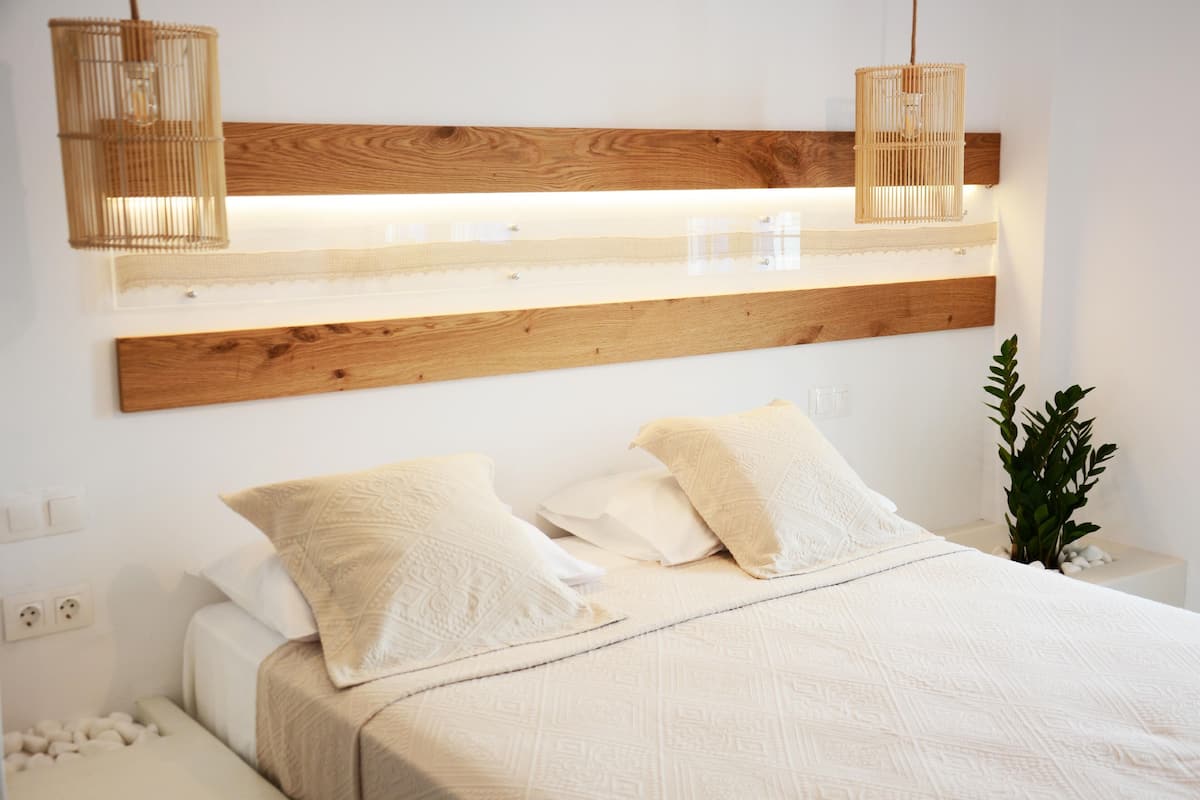 A bedroom with a wooden headboard, white bedding, and two hanging light fixtures.