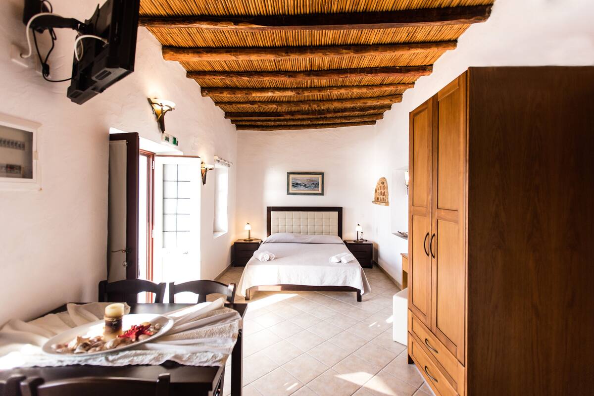 A bedroom with a bed, wooden wardrobe, bedside tables, and a dining area with a table and chairs.