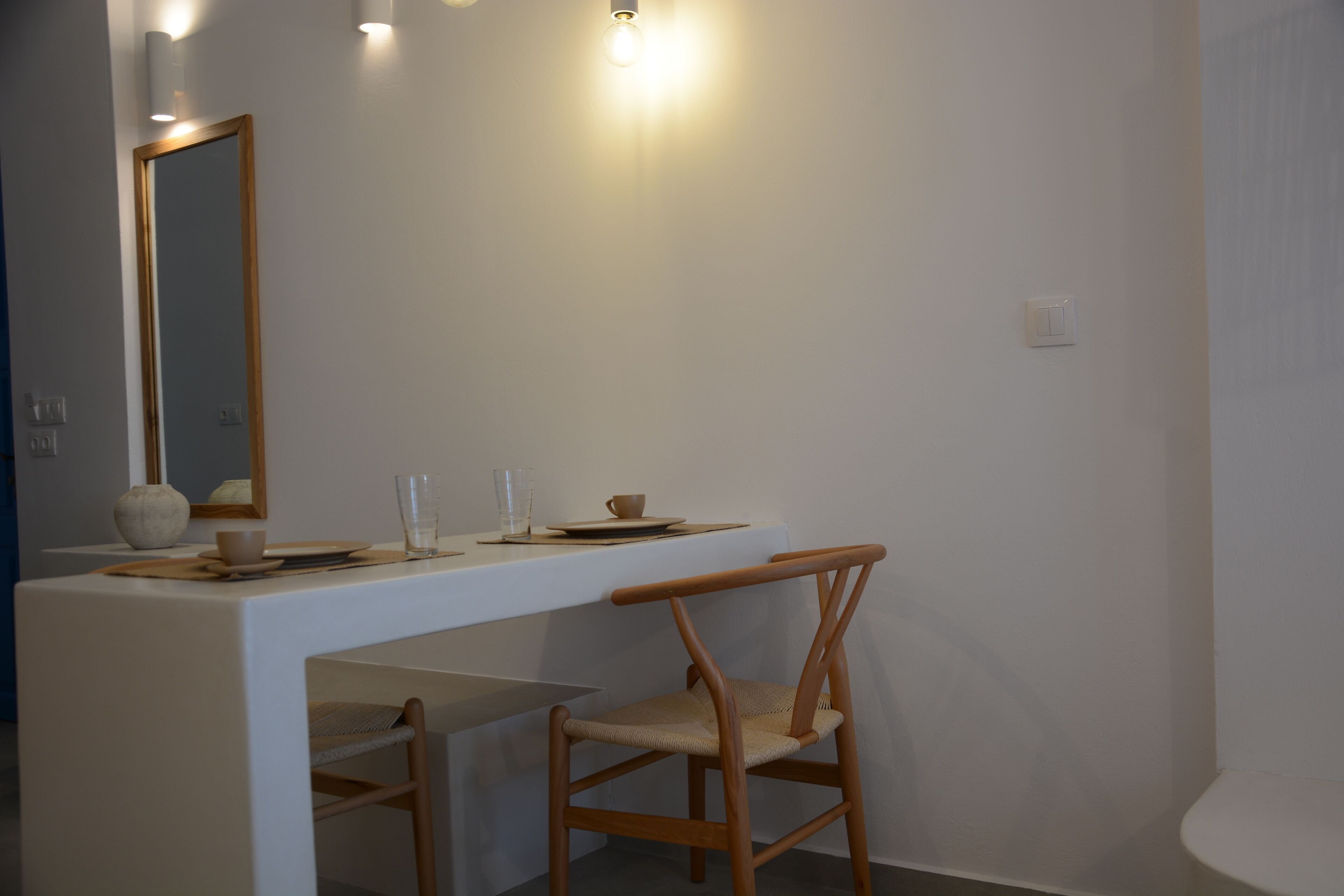 Una habitación minimalista con un escritorio blanco, una silla, un espejo y una lámpara.