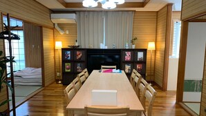 A spacious dining area with a long wooden table, surrounded by chairs, and a modern ceiling light fixture. - Nomu House (Chatan)