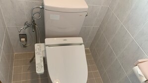 A modern bathroom with a toilet, bidet, and control panel. - Nomu House (Chatan)