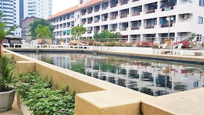 A swimming pool with a tiled edge, surrounded by potted plants and a building with multiple balconies in the background. - Plaza Residence Jomtien Beach (Pattaya)