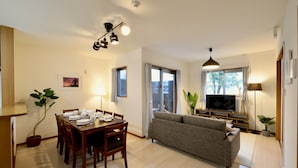 Ein modernes Wohnzimmer mit Essbereich, einer Couch, einem Fernseher und einer Deckenleuchte.