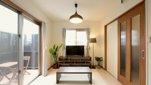 Ein Wohnzimmer mit Fernseher, einer Bank, einer Lampe und einer Schiebetür zum Balkon.