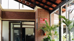 Entrada de un edificio con un cartel de extintor, un reloj y plantas en macetas.