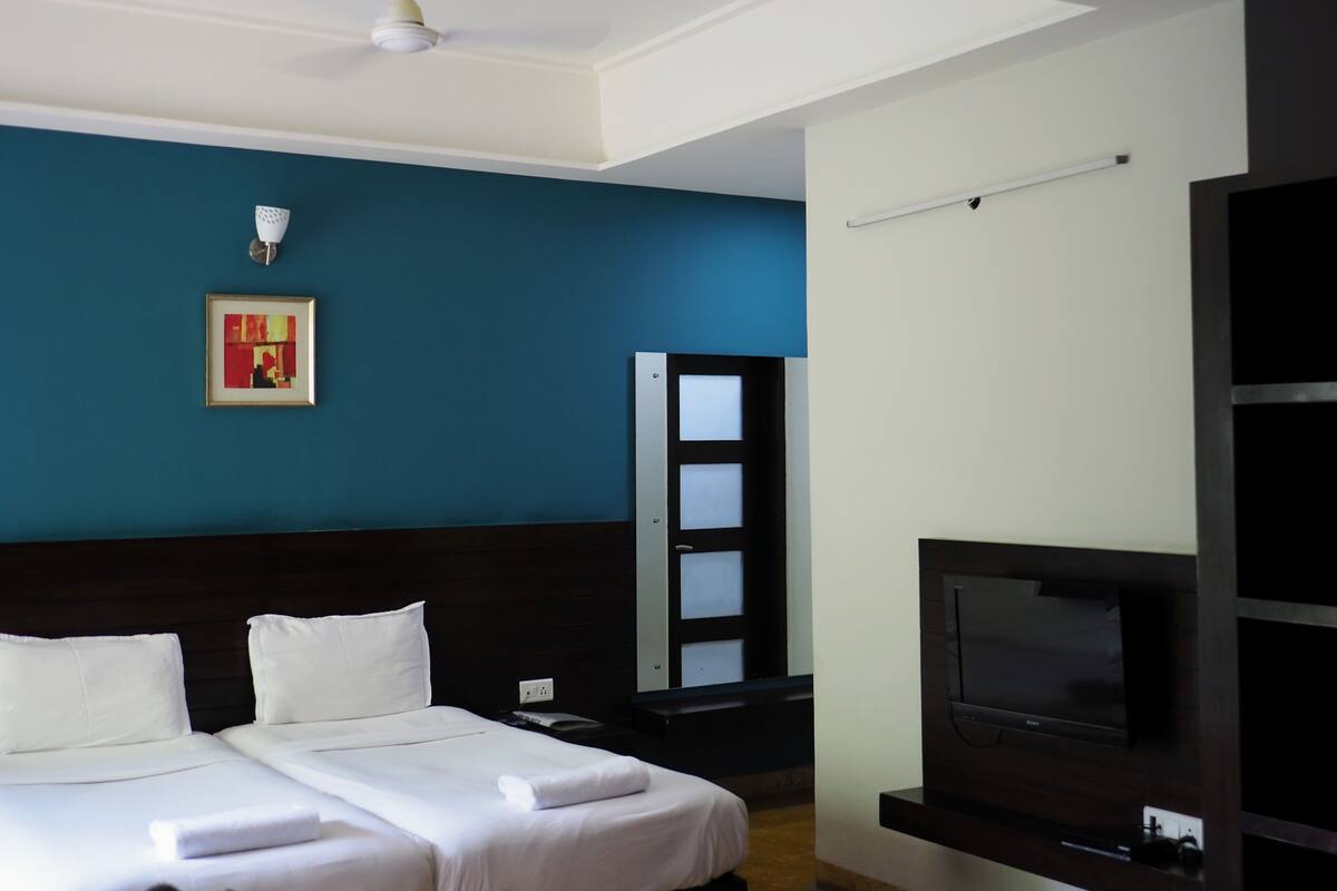 Een hotelkamer met twee bedden, een plafondventilator, een televisie en een schilderij aan de muur.