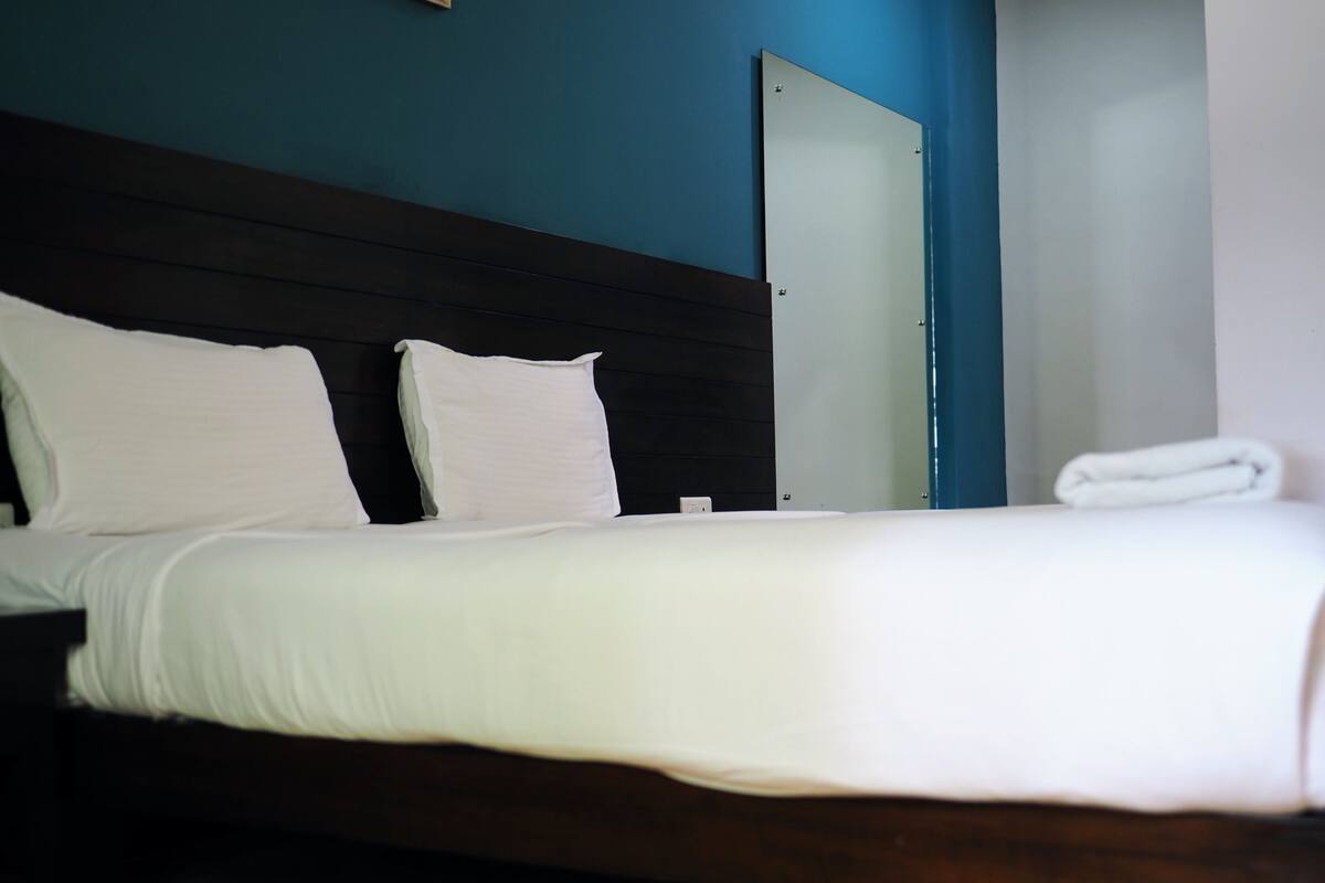 Een keurig opgemaakt bed met witte lakens in een kamer met een donker houten hoofdbord en een blauwe accentmuur.