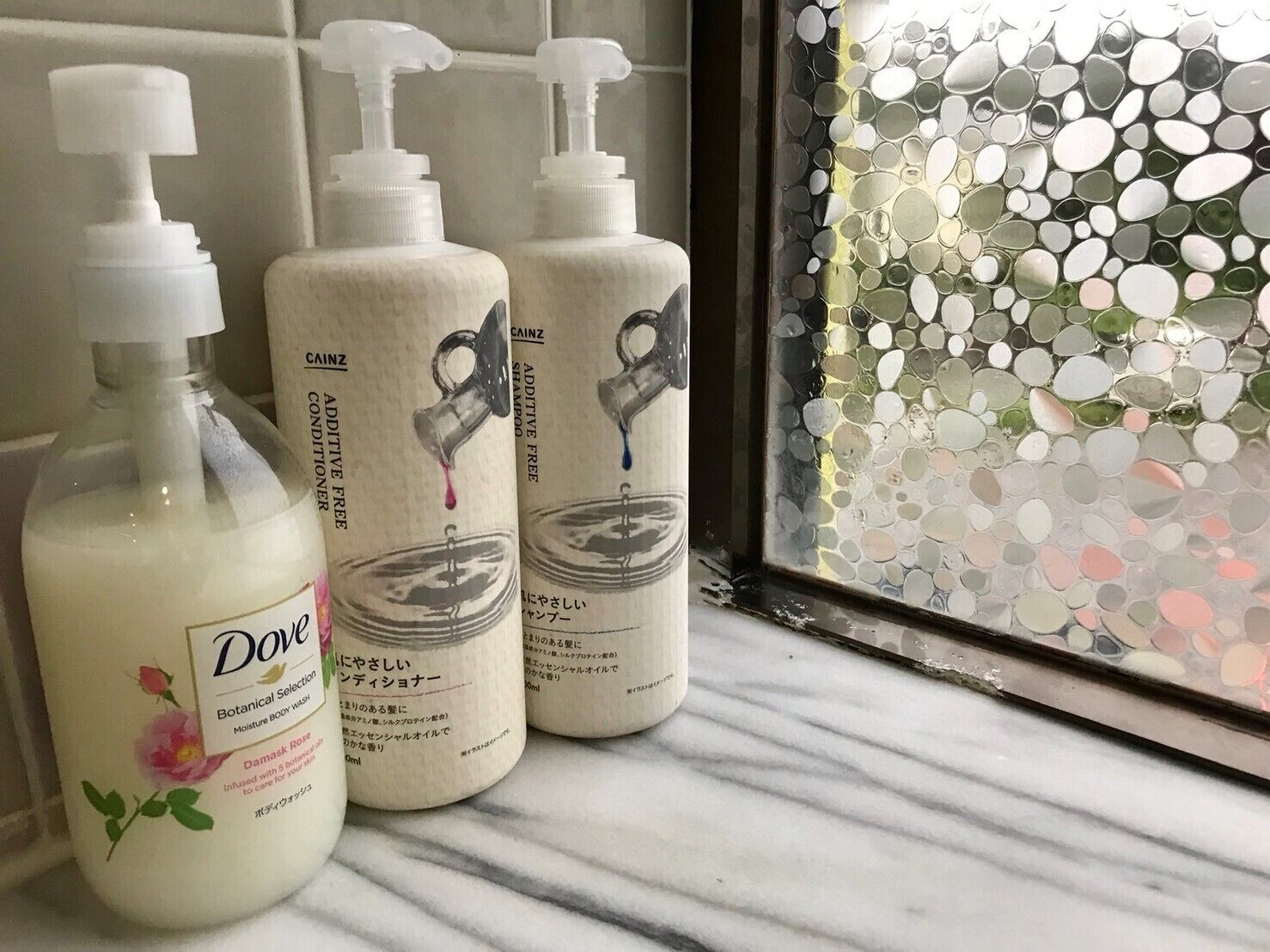 Three bottles of Dove body wash on a bathroom counter next to a mirror with a mosaic backsplash.