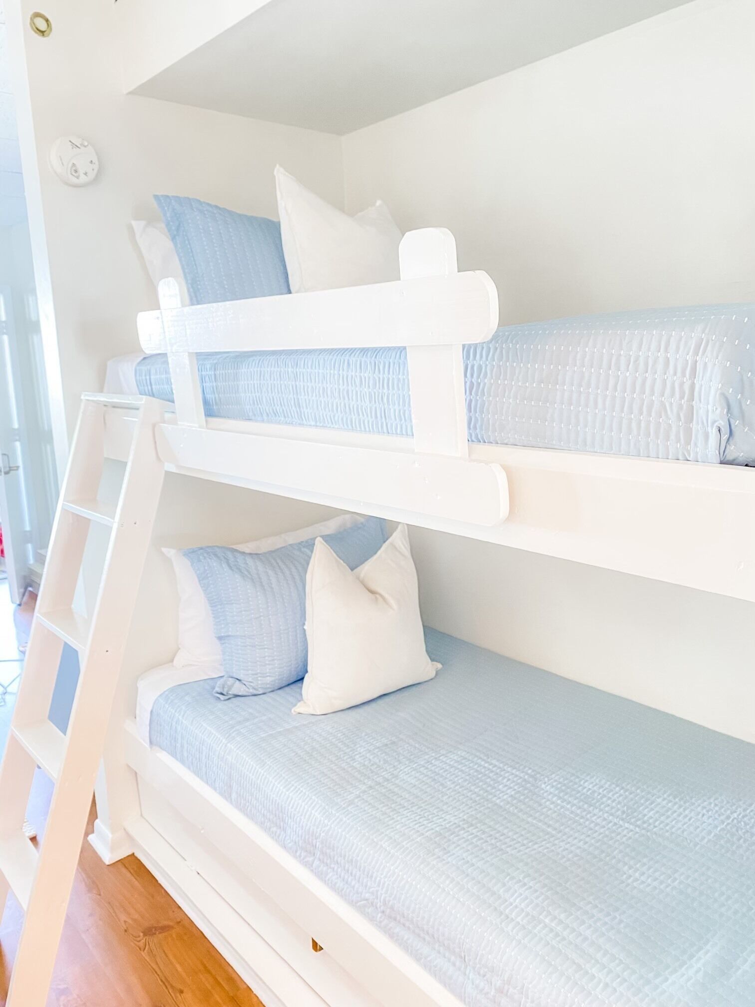 Un lit superposé avec une échelle, des murs blancs et une petite fenêtre.