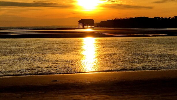A sunset over a beach with a pier extending into the water.