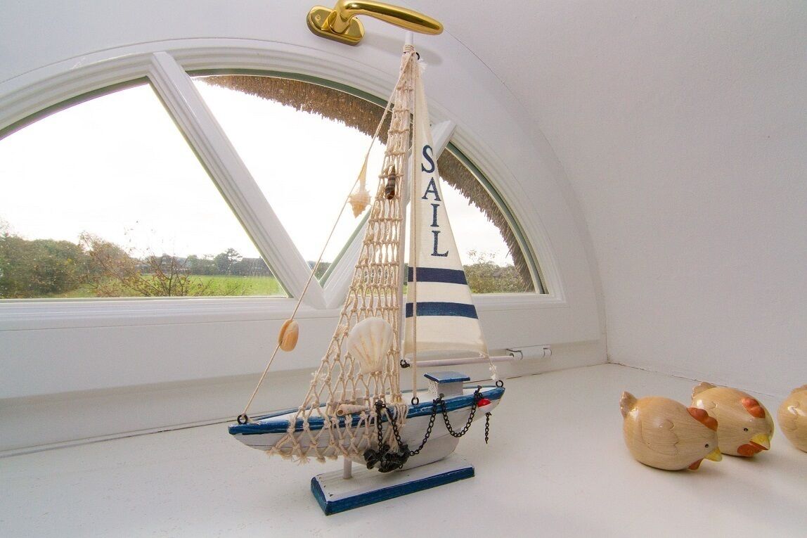 En modelsejlads med ordet "Sail" på sejlet, placeret på et vindueskar med grøn vegetation udenfor.