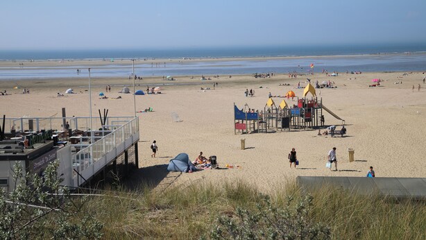 A beach with a playground, tents, and a lifeguard tower.