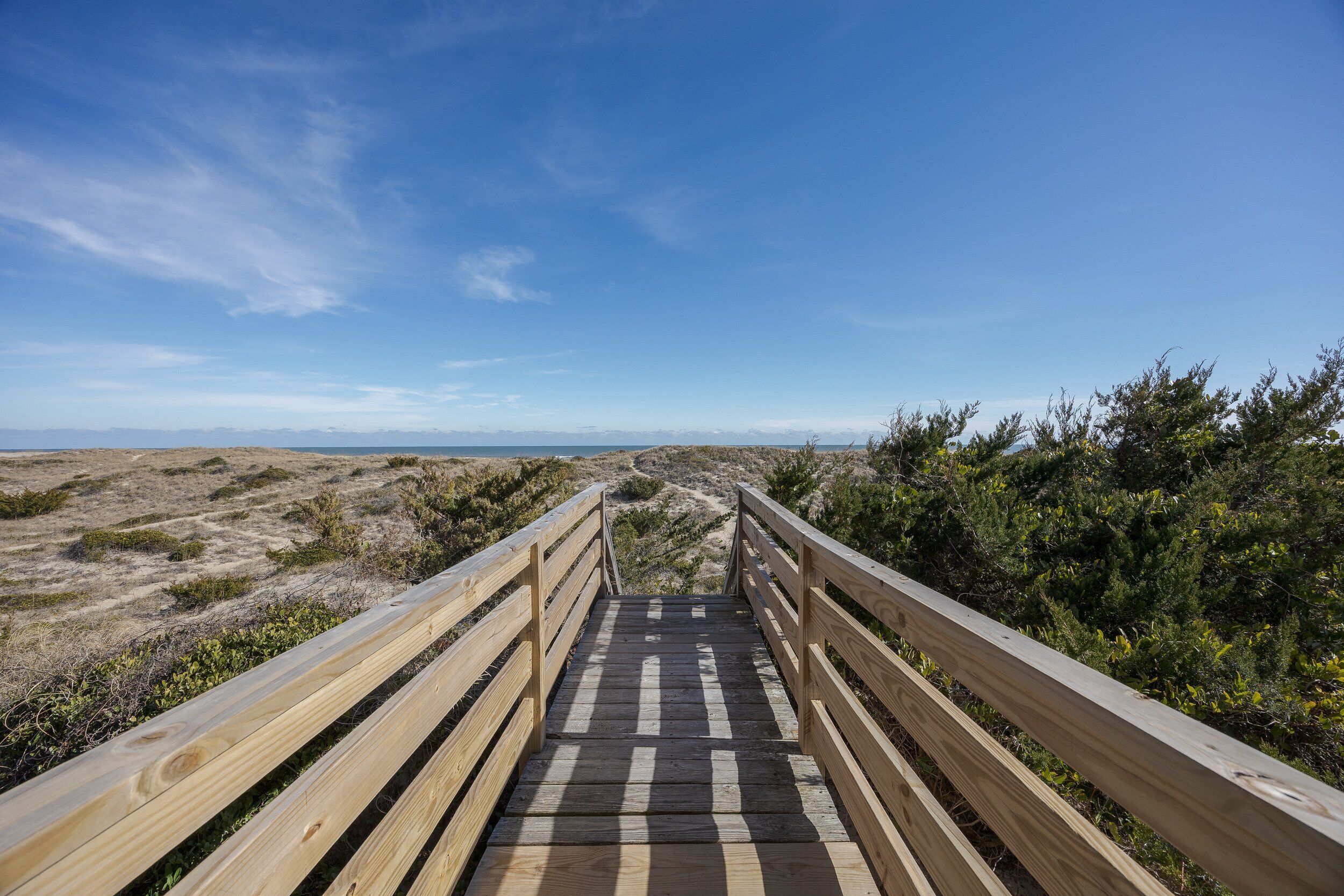 A wooden boardwalk leading to a beach with a clear sky.