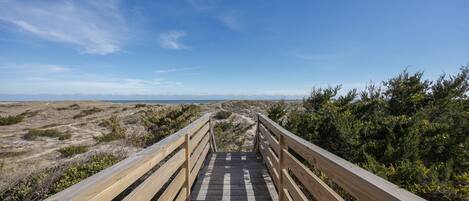 A wooden boardwalk leading to a beach with a clear sky.