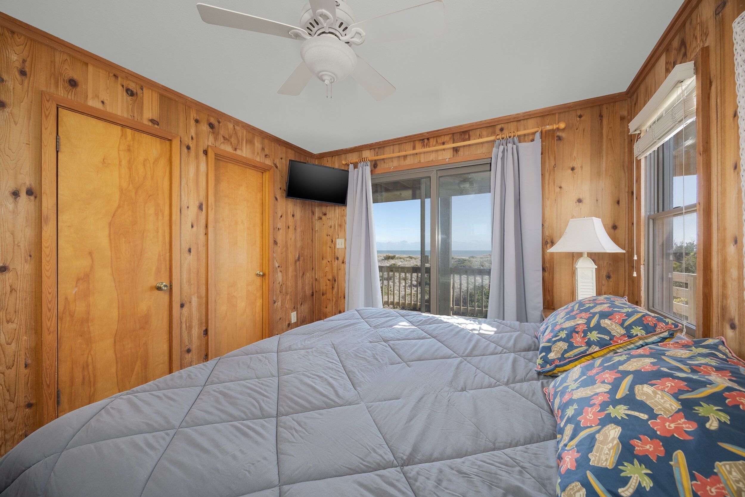 Une chambre à coucher avec un lit, un ventilateur de plafond, des murs en bois, une télévision et une fenêtre avec des rideaux.