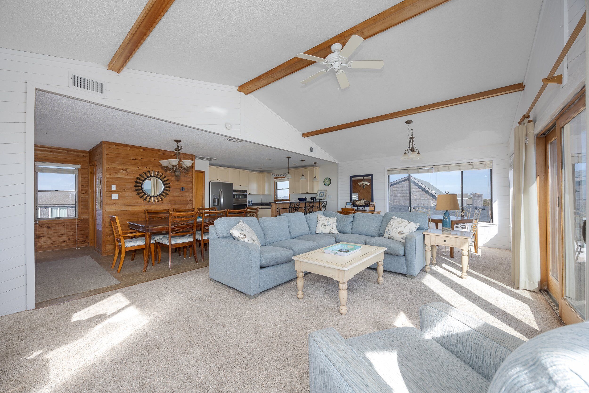 A spacious living room with a large sectional sofa, a coffee table, and a dining area with wooden chairs and a table.