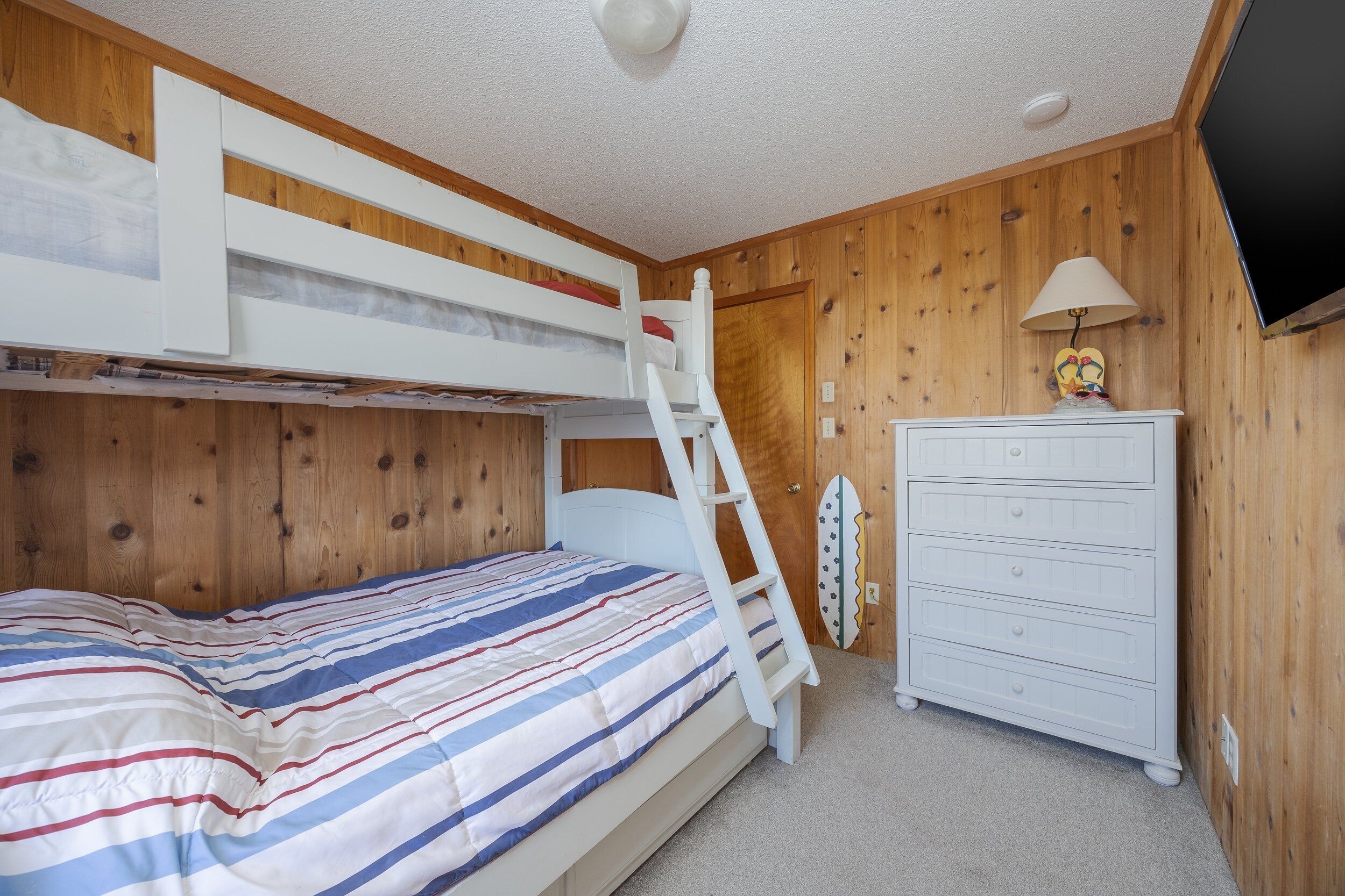 A bunk bed with a ladder, a dresser, and a surfboard against the wall.