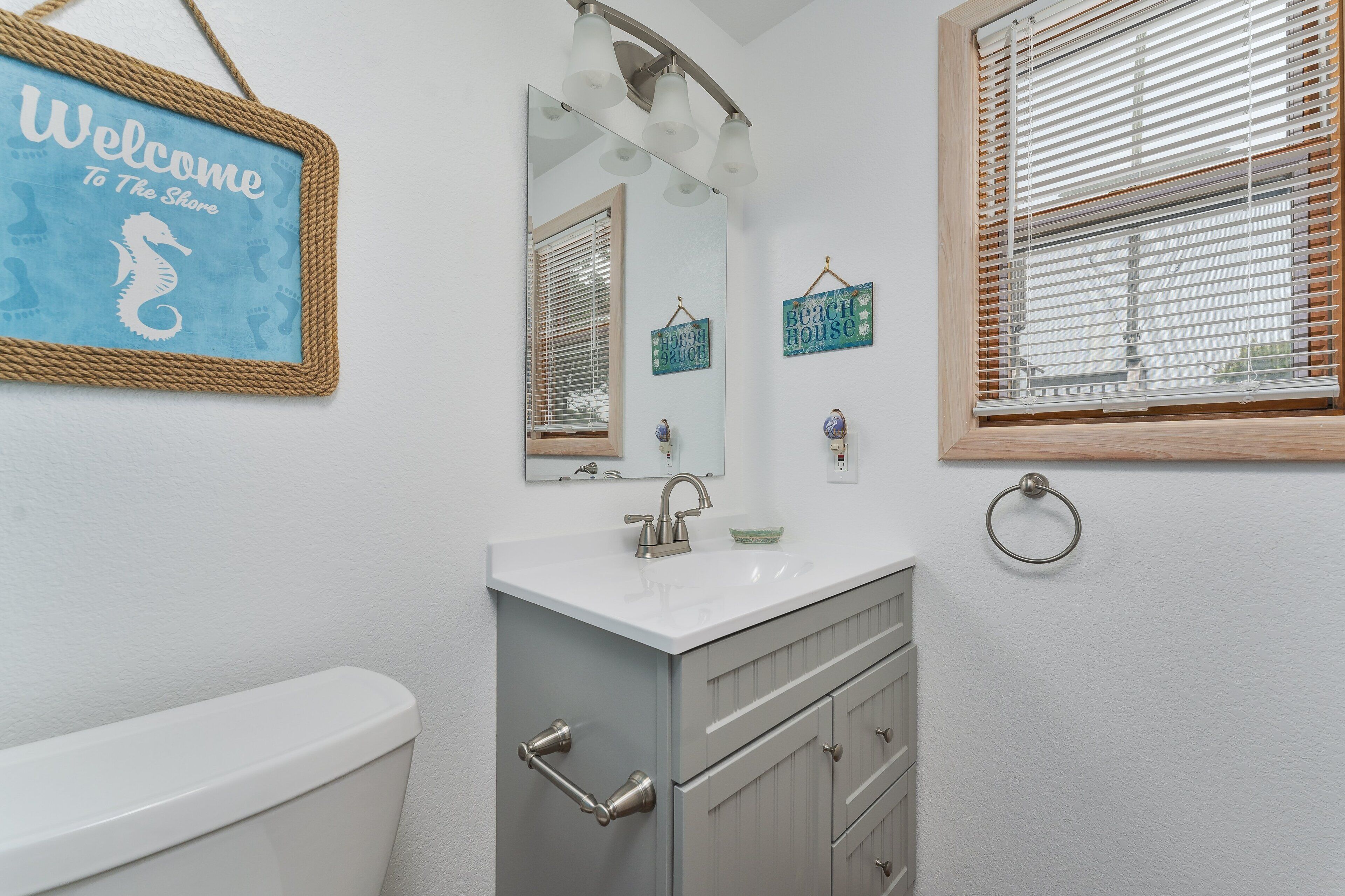 A bathroom with a white sink, a mirror, a toilet, and a window with blinds.