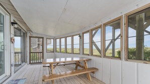 Een overdekt terras met een houten picknicktafel en banken, grote ramen en uitzicht op de omgeving.