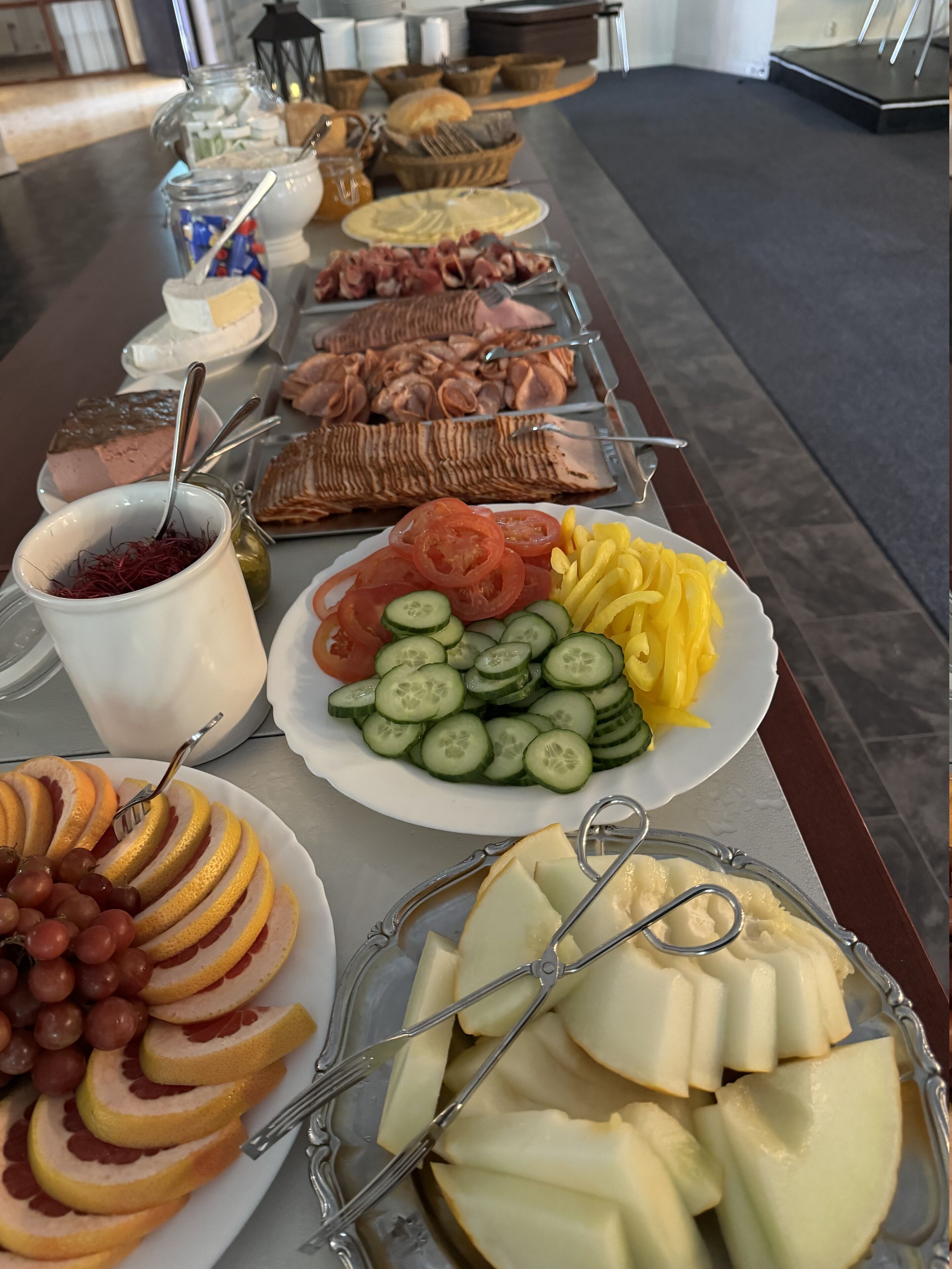 Una mesa de buffet con diversas opciones de comida, incluyendo frutas cortadas, quesos y carnes.