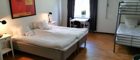 A hotel room with a bed, a desk, a chair, a bunk bed, and a window with curtains.