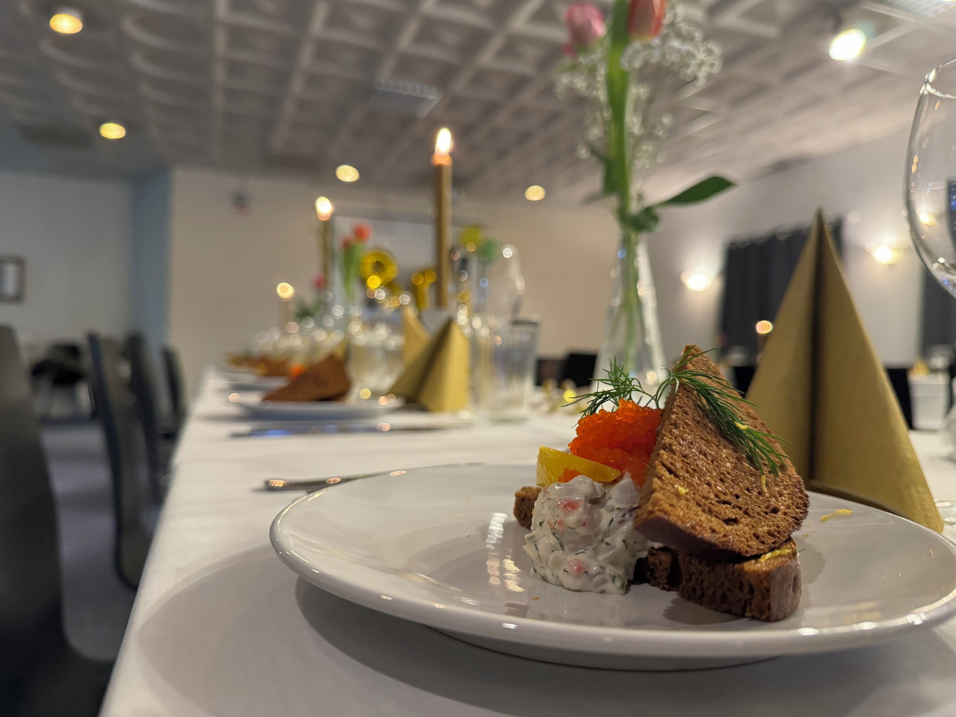 Una mesa de comedor con un plato de comida, que incluye una rebanada de pan con decoración, una porción de queso crema con hierbas y un pequeño recipiente de caviar.