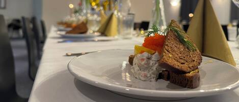Una mesa de comedor con un plato de comida, que incluye una rebanada de pan con decoración, una porción de queso crema con hierbas y un pequeño recipiente de caviar.