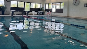 An indoor swimming pool with clear lanes, a clock, and windows with a view of trees.