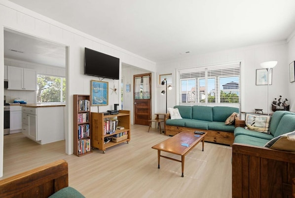 A living room with a green sofa, a coffee table, a bookshelf, and a TV mounted on the wall.