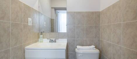 A bathroom with a white sink, mirror, and toilet, tiled in a light beige color.