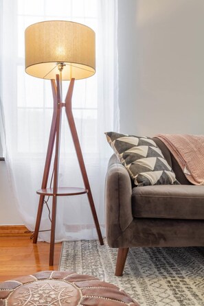 Un lampadaire doté d’un abat-jour texturé, un canapé agrémenté de coussins à motifs et un pouf décoratif.