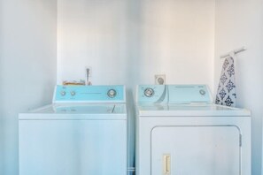 Une buanderie équipée de deux machines à laver, une bleue et une blanche, ainsi que d’un porte-serviettes sur lequel est posée une serviette à motifs.