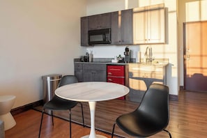A modern kitchen with dark cabinets, a microwave, and a red dishwasher. There is a round table with two black chairs in the foreground.