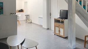 Amplia sala de estar con una escalera, una mesa de comedor y un televisor sobre un mueble de madera.