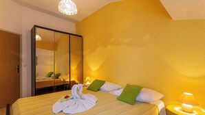 A hotel room with two beds, a large mirror, a round yellow nightstand with a lamp, and a wooden door. - Milka in Medulin - Istrien / Milka in Medulin - Appartement für 2-4 Personen (Medulin)