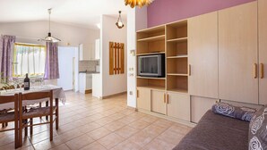 A living room with a sofa, a TV on a wooden stand, a dining table with chairs, and a kitchen in the background. - Milka in Medulin - Istrien / Milka in Medulin - Appartement für 2-4 Personen (Medulin)