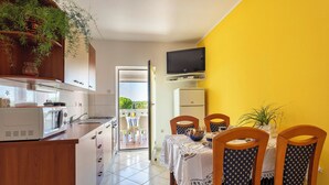 A compact kitchen with a dining area, a TV mounted above the counter, and a view through the open door to an outdoor patio.