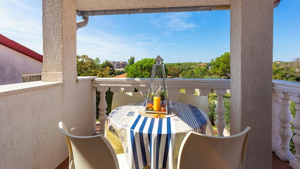 A balcony with a table set for two, a clear view of the surrounding landscape, and a white balustrade.