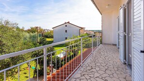 A balcony with a stone floor, white railing, and a view of a house and greenery.