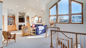 A spacious living room with a fireplace, a large window, and a staircase. - 4052 - Mirth N Mist II - Spacious Duck Escape | Pool & Sleeps 17 (Duck)