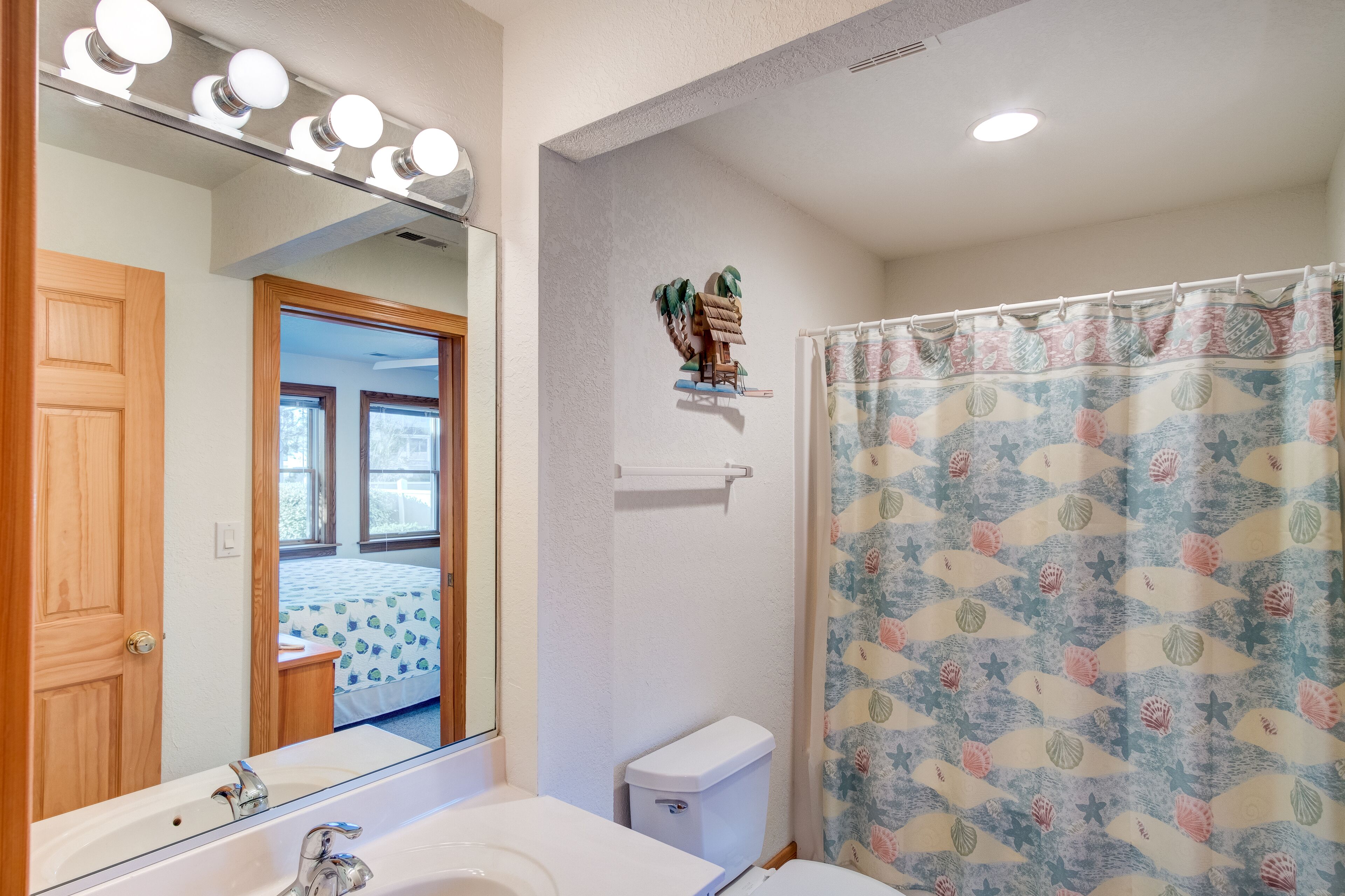 A bathroom with a mirror, vanity, sink, toilet, and shower curtain.