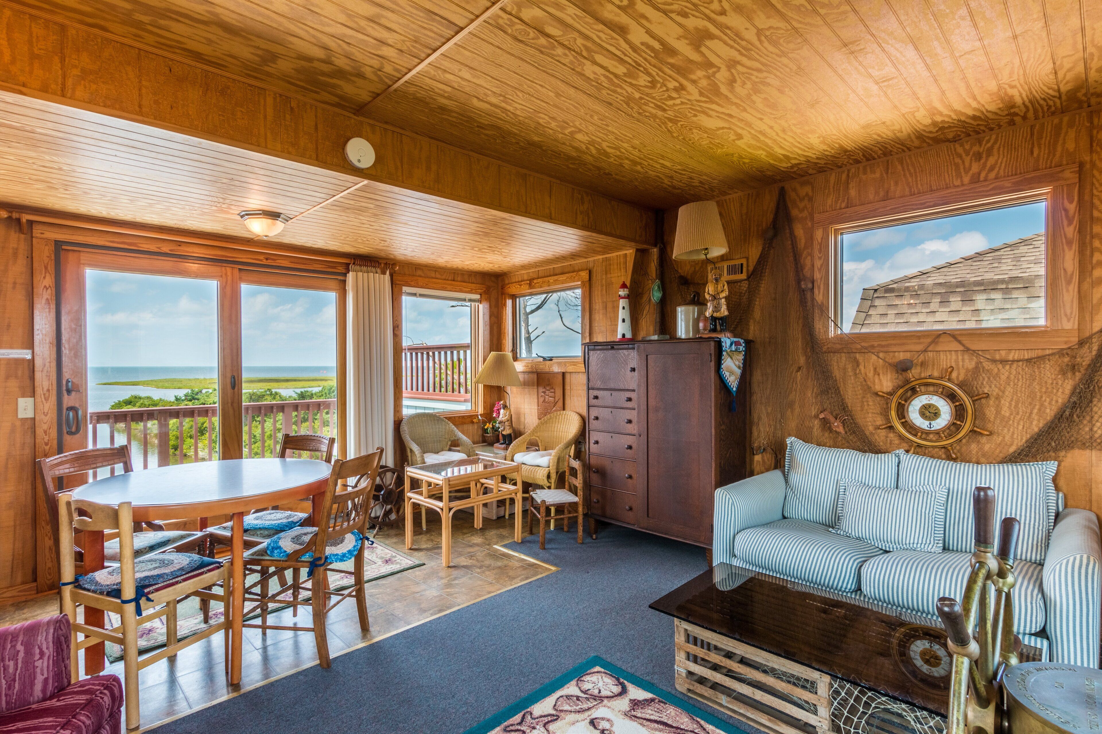 A wooden interior with a dining area, a sofa, and a view through large windows.