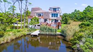 Ein zweistöckiges Haus mit einem Steg, der in einen Teich führt, umgeben von üppiger Vegetation.