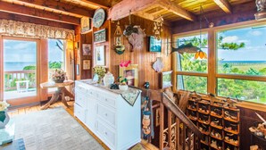 Ein rustikales Blockhaus-Interieur mit Holzbalken, einem großen Fenster mit Blick auf Grünflächen, einer weißen Kommode und verschiedenen Dekorationen.