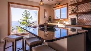 A kitchen with a large island, bar stools, pendant lights, and a view of trees and mountains. - 6BR Mtn House, Spectacular Valley and Sunset Views, Rec Room, Hot Tub, Fire Pit (Snowshoe)