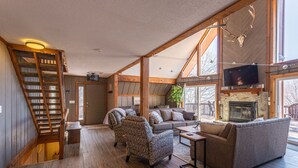 A spacious living room with a fireplace, a television, and a staircase. - 6BR Mtn House, Spectacular Valley and Sunset Views, Rec Room, Hot Tub, Fire Pit (Snowshoe)
