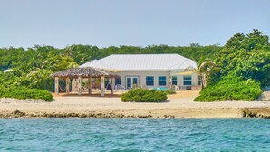 A beachfront property with a thatched-roof structure, a pool, and lush greenery.