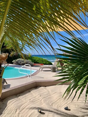 A poolside area with a clear view of the ocean, surrounded by sand and palm trees. - Luxury Oceanfront Cayman Brac Escape, Private Pool, 3BR Stunning Caribbean Views (Stake Bay)